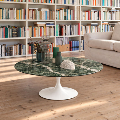 erde Imperial Tulip coffee table featuring a polished Alpi Green marble tabletop with striking white veining, paired with a glossy white tulip pedestal base. Styled in a contemporary living room with a bookcase, light wood flooring, decorative glass vases, and a cream sofa, showcasing luxury Italian design for modern, Scandinavian, and mid-century interiors.