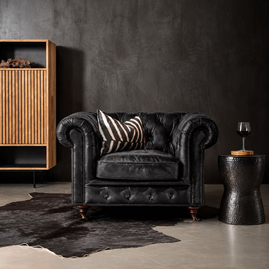 Vintage black Chesterfield leather armchair with deep diamond button tufting, rolled scroll arms, antique brass nailhead trim, turned wooden legs with castors, and luxurious British-inspired design for elegant living rooms, offices, and hotel lounges.