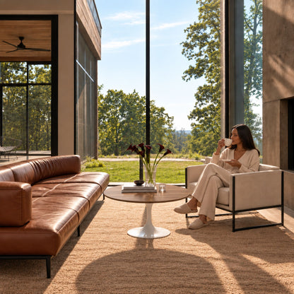 Walnut Essence Tulip coffee table featuring a natural walnut wood tabletop and glossy white tulip pedestal base, styled in a contemporary living room with a tan leather sofa, modern armchair, floor-to-ceiling windows, and warm natural light. A luxury Italian designer coffee table for modern, Scandinavian, and mid-century interiors.