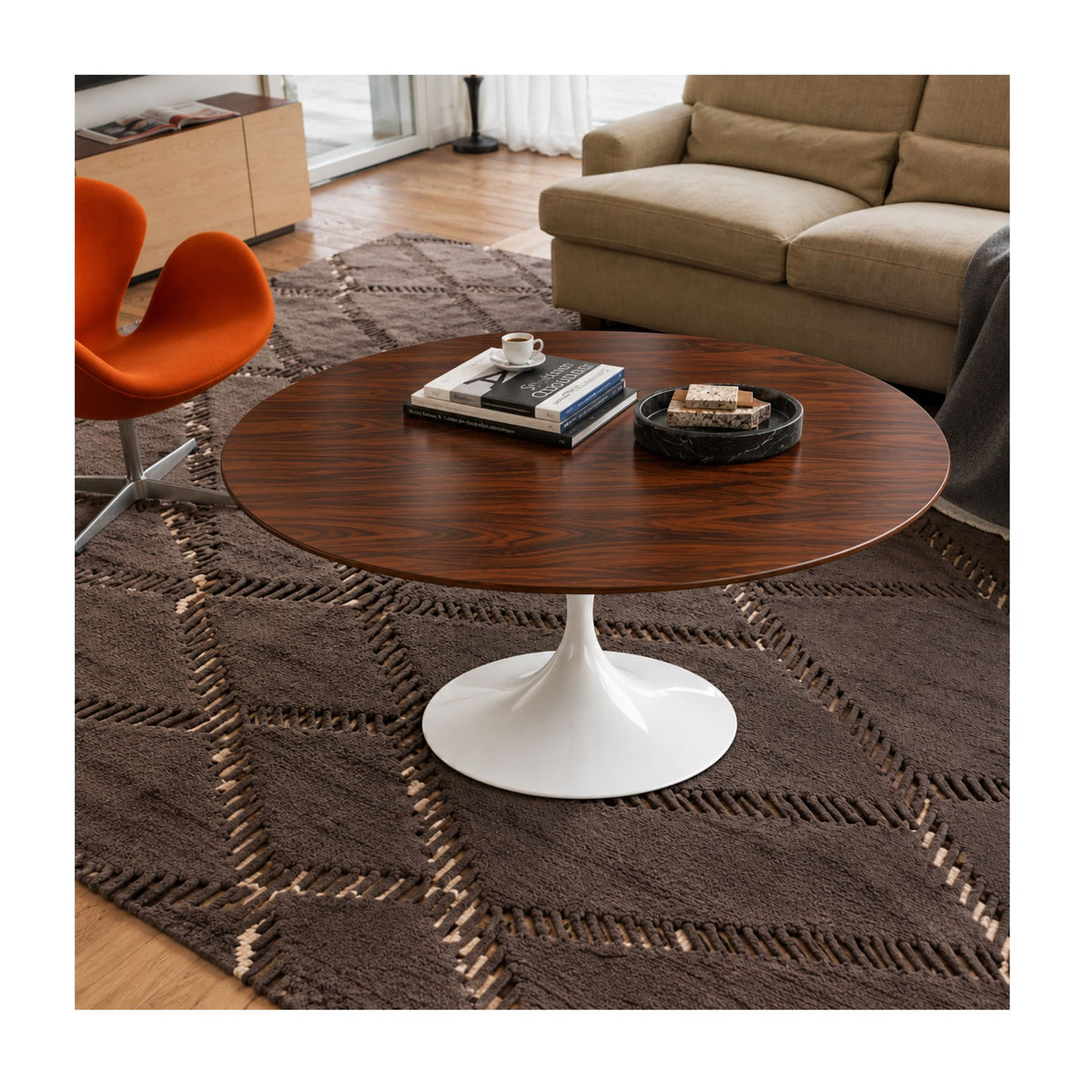 Walnut Prestige Tulip coffee table featuring a premium American walnut veneer round tabletop paired with a glossy white tulip pedestal base. Styled in a contemporary living room with a beige sofa, orange accent chair, textured rug, books, coffee cup, and decorative tray, showcasing timeless Italian design for modern, Scandinavian, mid-century, and minimalist interiors.