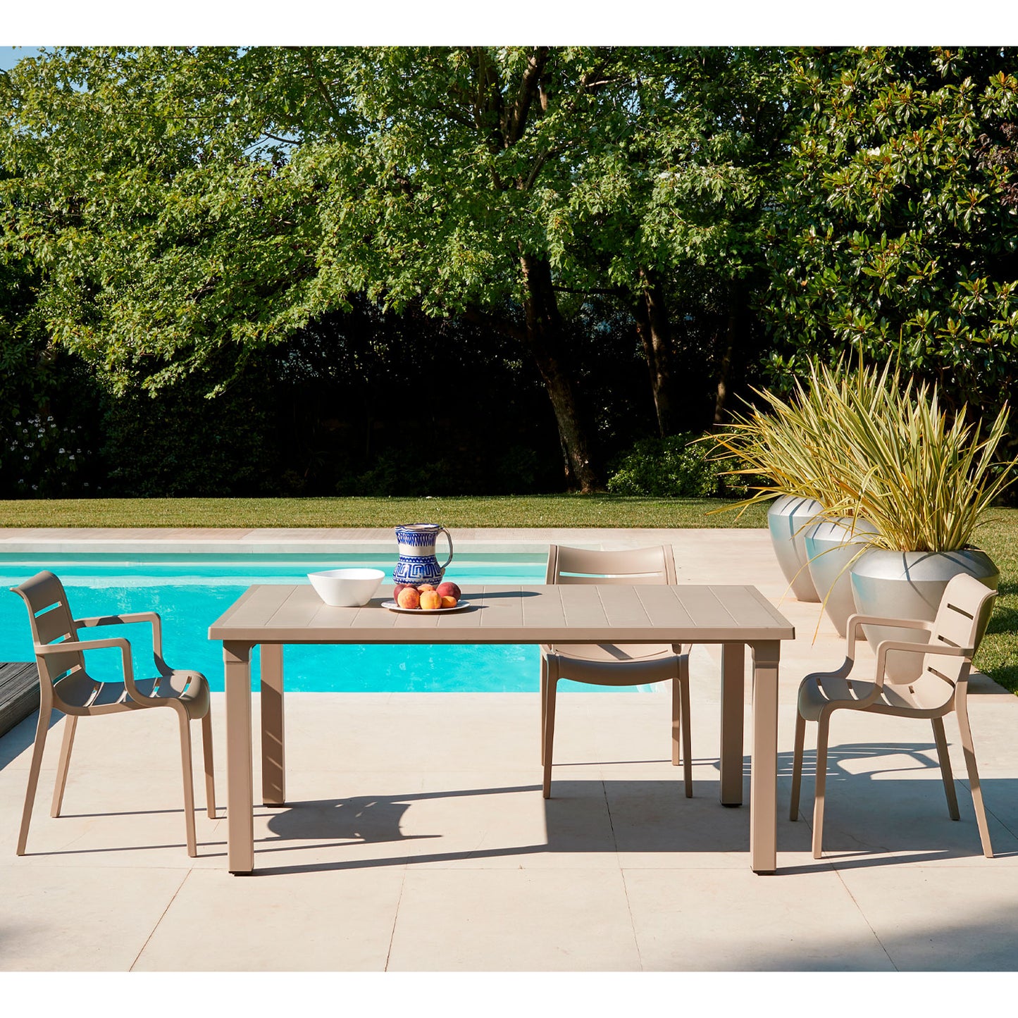 SCAB Sunset outdoor armchairs paired with a matching dining table beside a swimming pool, creating a modern Italian garden dining space for patios, terraces and hospitality settings.